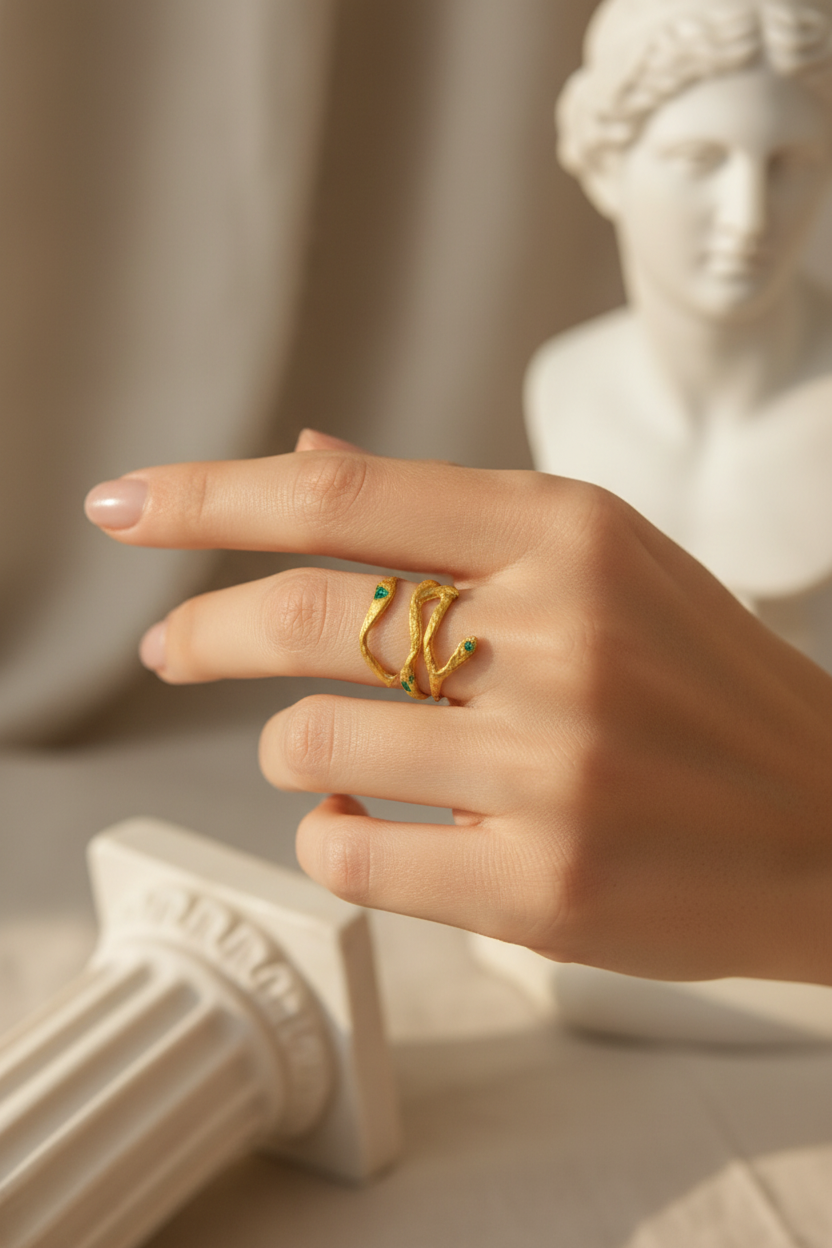 Hand wearing a gold ring with green gemstones in front of a classical statue.