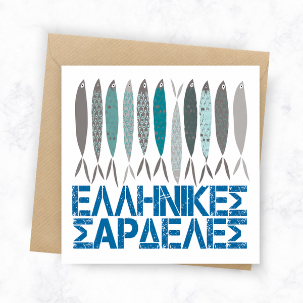 A square greeting card with a kraft paper envelope, featuring a row of stylized fish in gray, teal, and blue patterns above the Greek text 'ΕΟΛΩΝ ΓΑΒΕΛΕ' in distressed blue lettering, set on a light marble background.