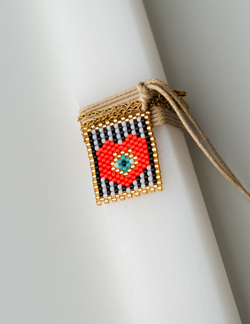 Decorative beaded pendant with a red center and gold frame on a white background