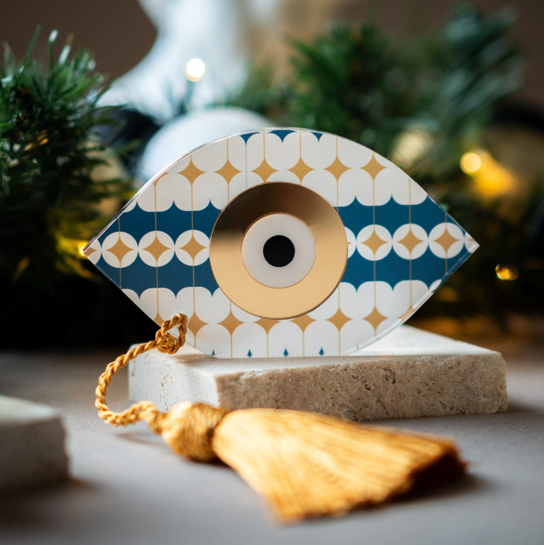 Decorative eye ornament with gold tassel on a neutral background