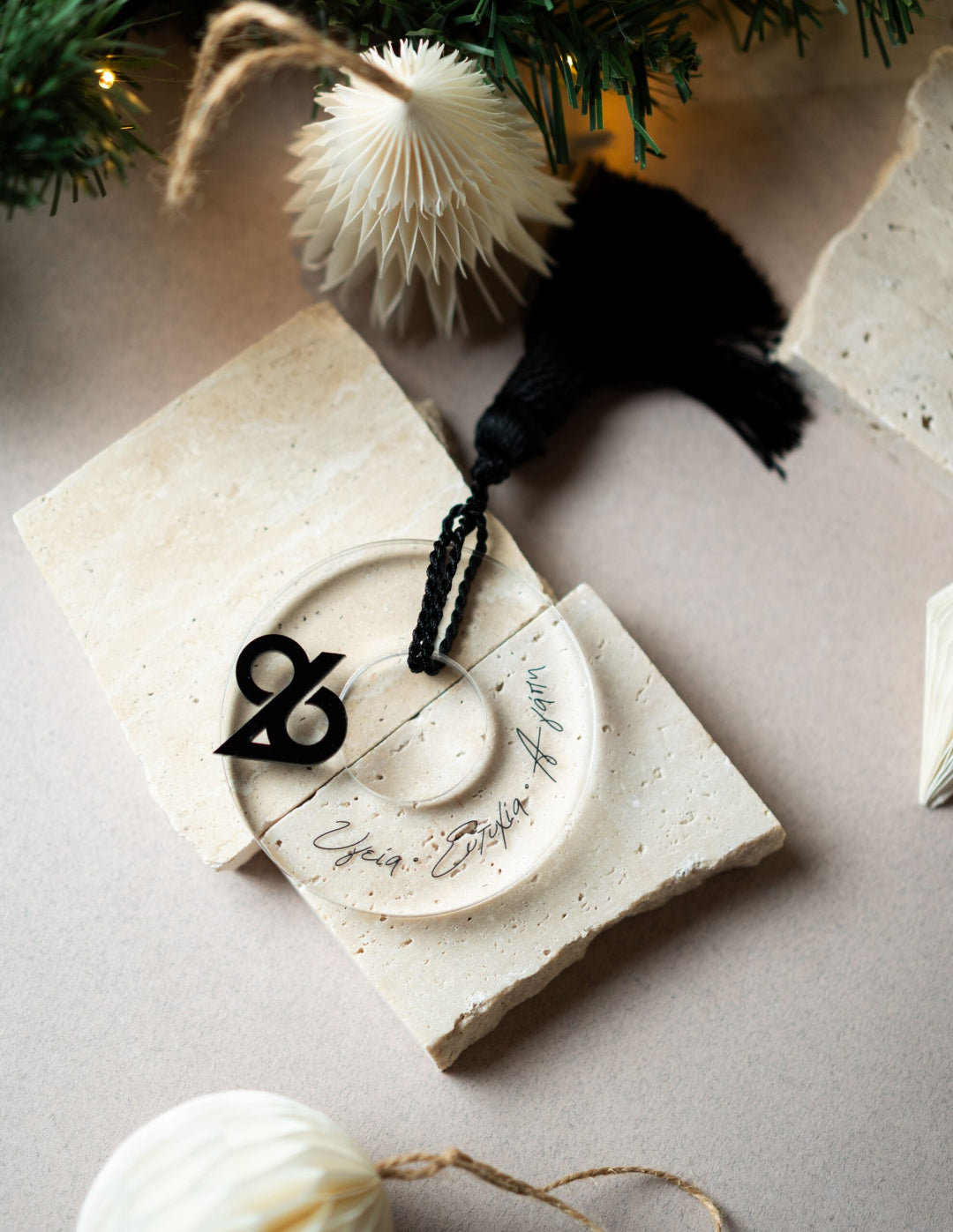 Decorative stone with a circular design and black ampersand symbol, surrounded by Christmas ornaments on a light surface.