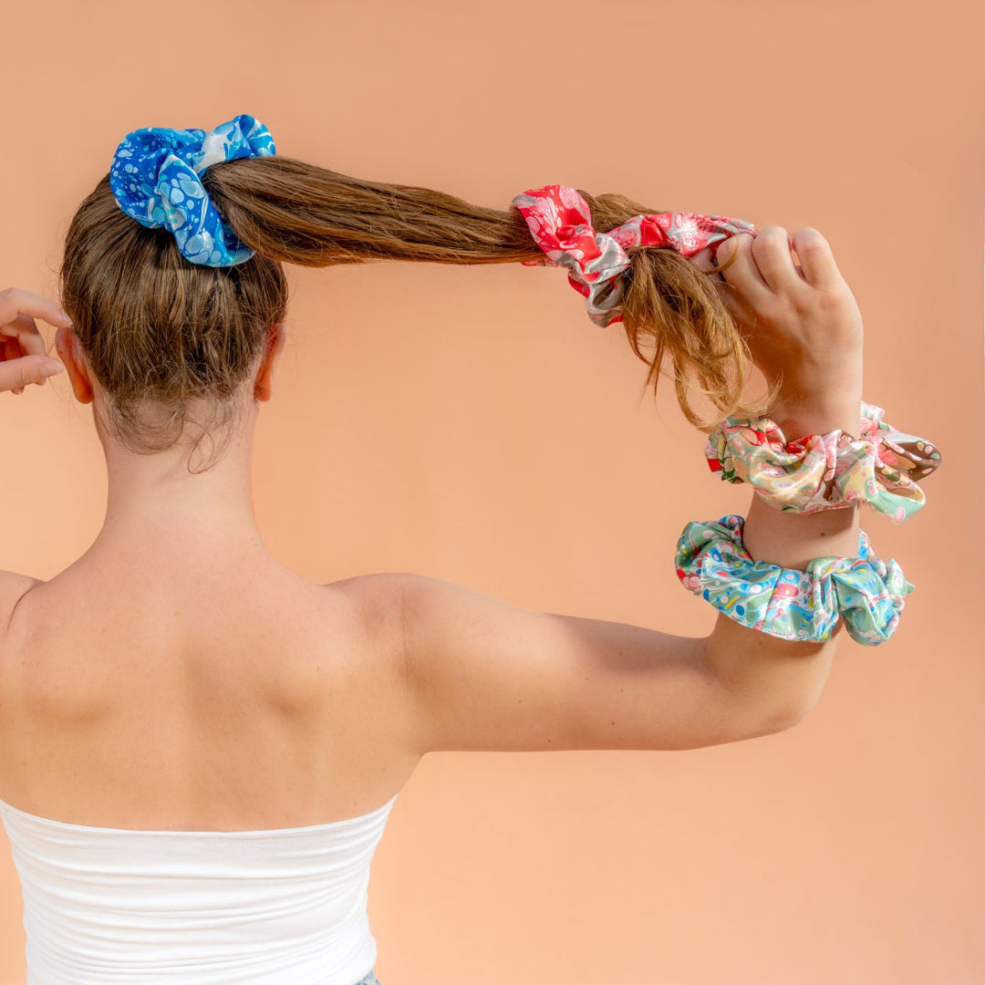 Woman styling her hair with colorful scrunchies on a peach background