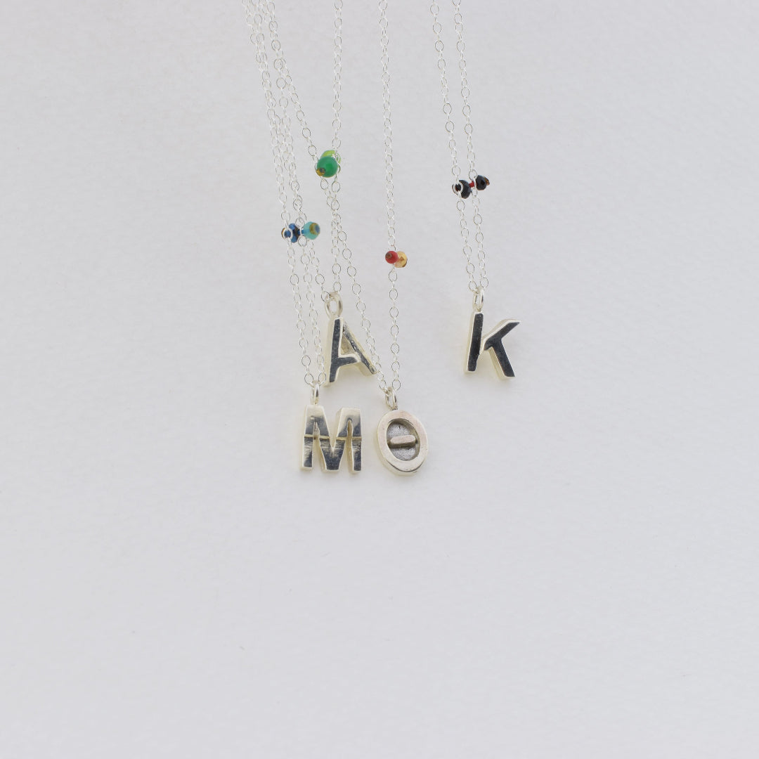 Two silver necklaces with letter pendants on a light gray background