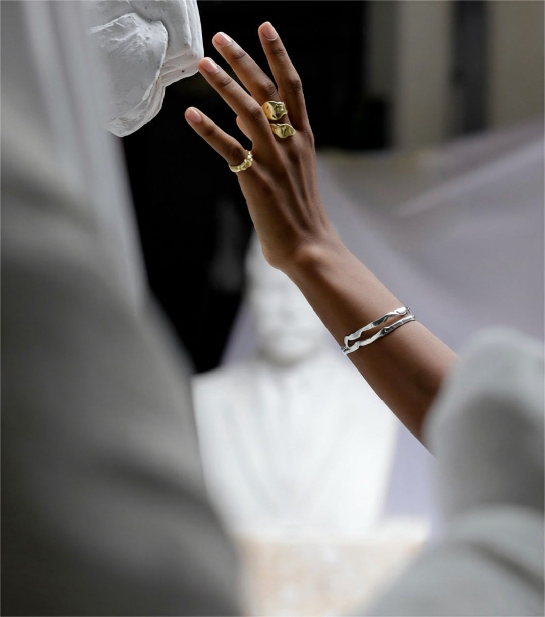 Hand wearing a gold ring and silver bracelet with a blurred background