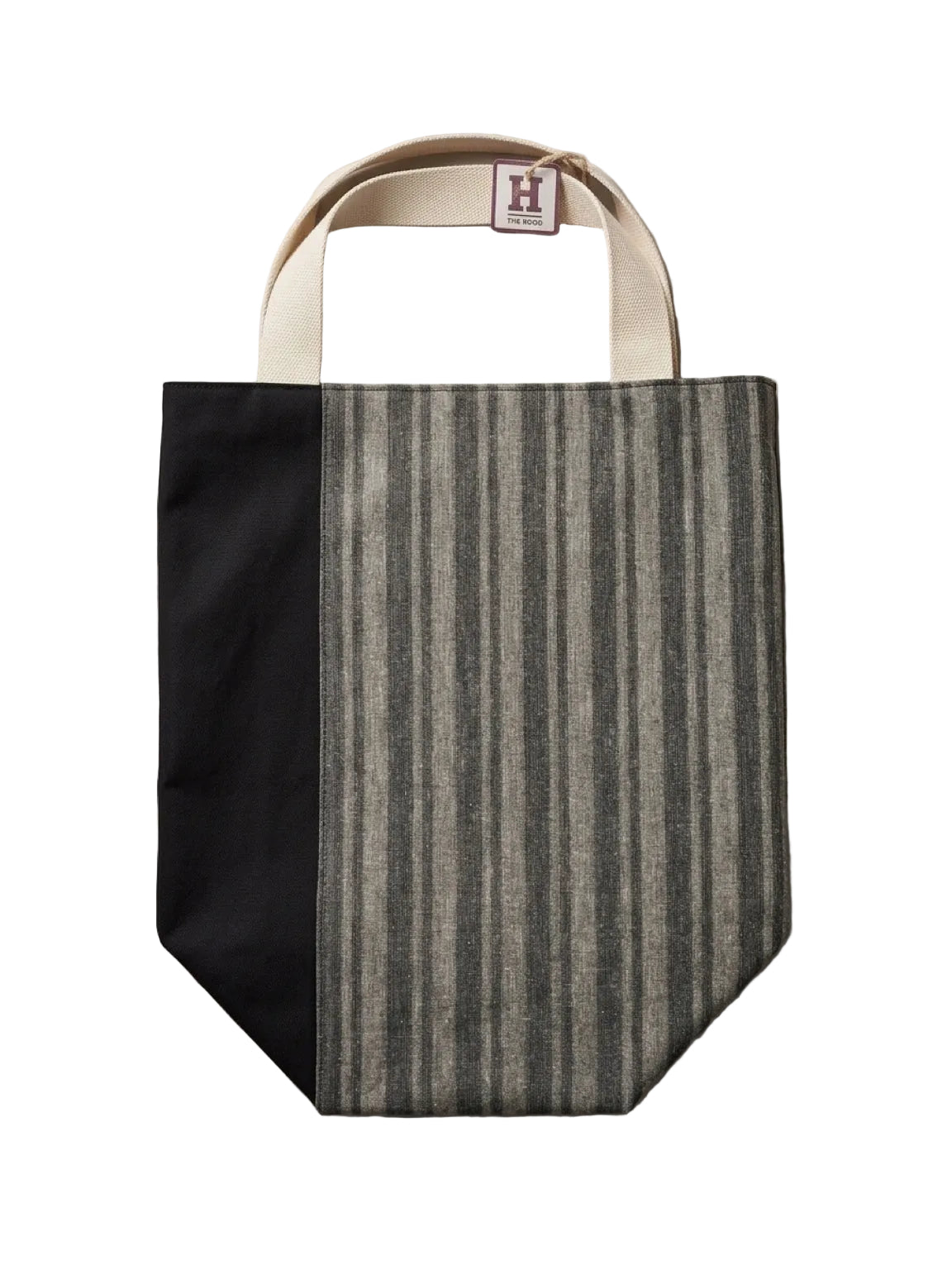 A tote bag with a black left panel and a gray and beige vertically striped right panel, featuring cream-colored handles and a small brand tag at the top.