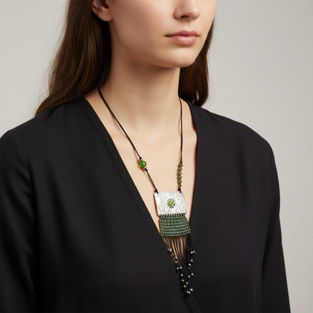 Woman wearing a black top with a long, decorative necklace featuring green beads and a silver pendant.