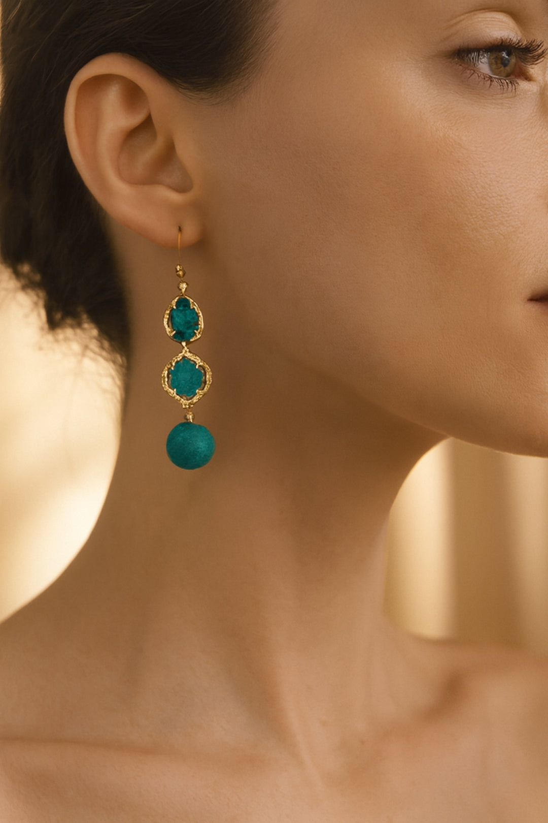 Close-up of a woman wearing turquoise earrings with gold accents.