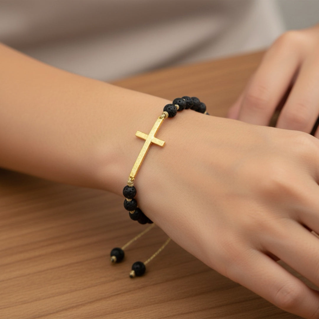 Gold cross bracelet with black beads on a wrist against a wooden surface