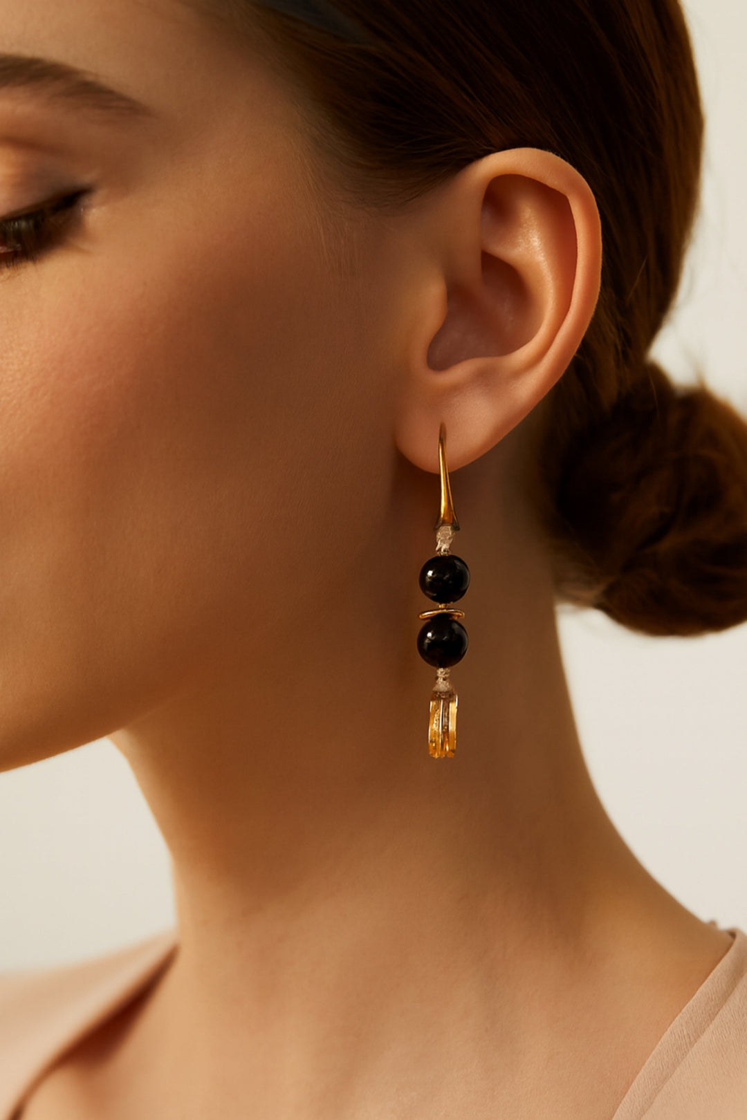 Close-up of a woman wearing a gold earring with black beads against a neutral background