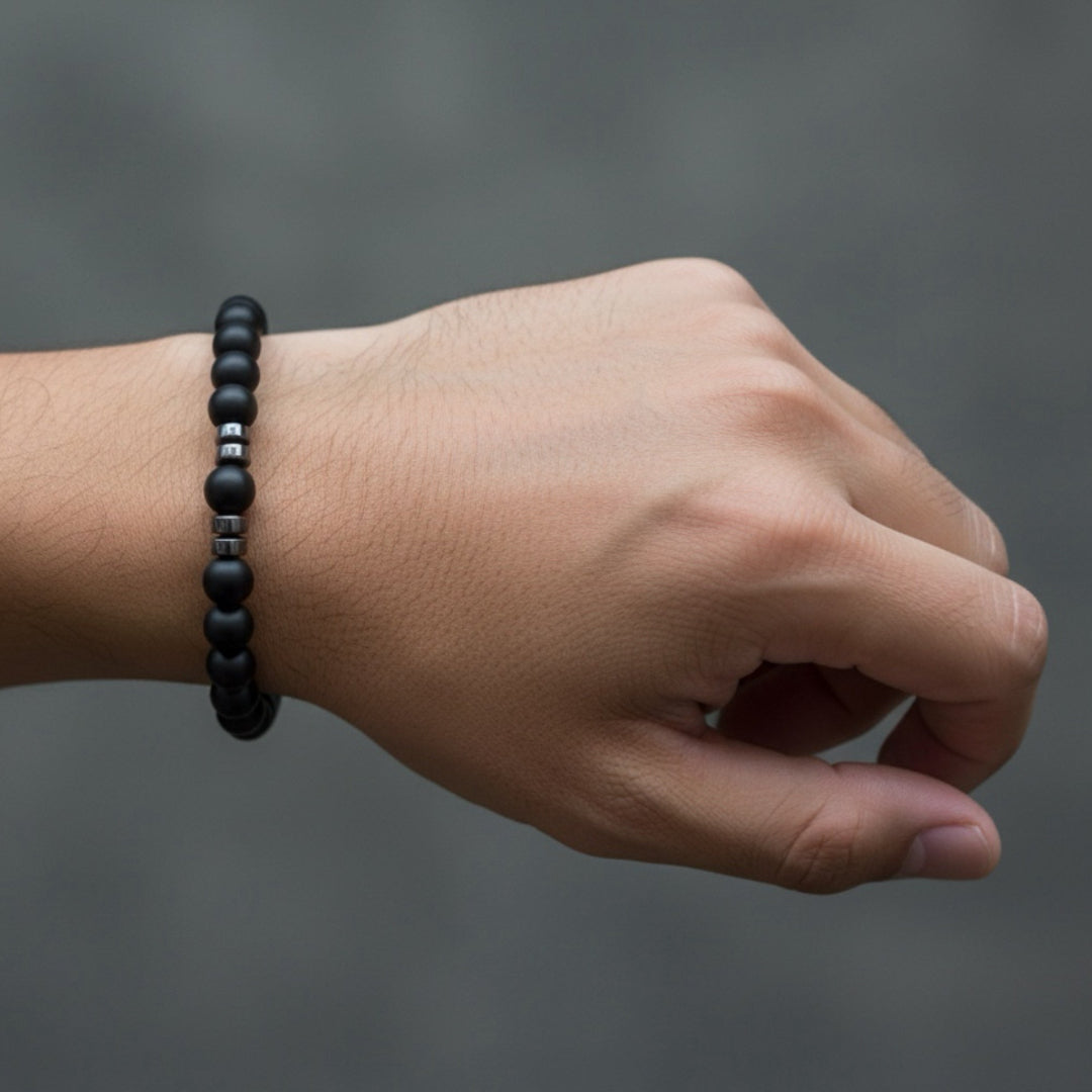 Hand wearing a black beaded bracelet on a gray background