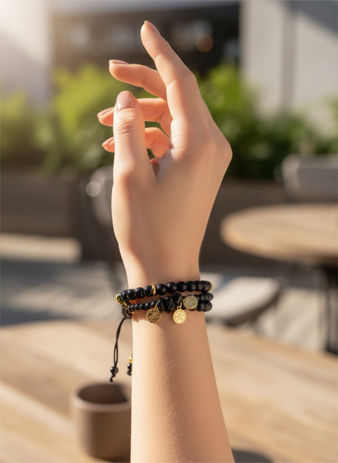 Hand wearing two bracelets with a blurred outdoor background