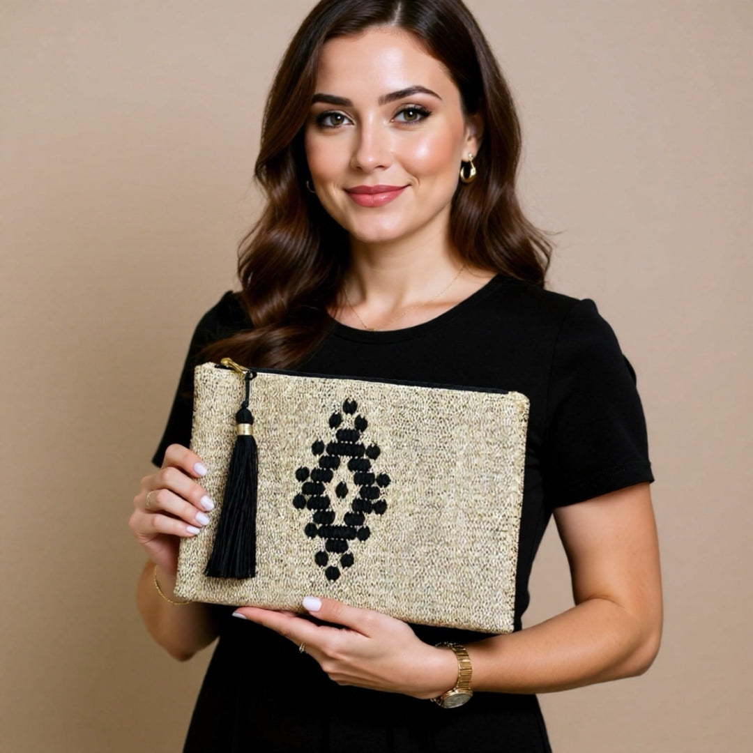 Woman holding a gold clutch with black design and tassel against a beige background