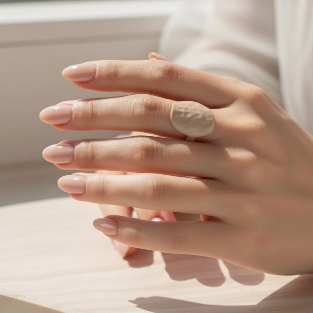 Close-up of a hand wearing a beige ring on a neutral background