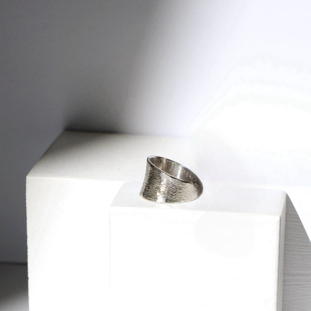 Silver ring on a white pedestal against a gray background
