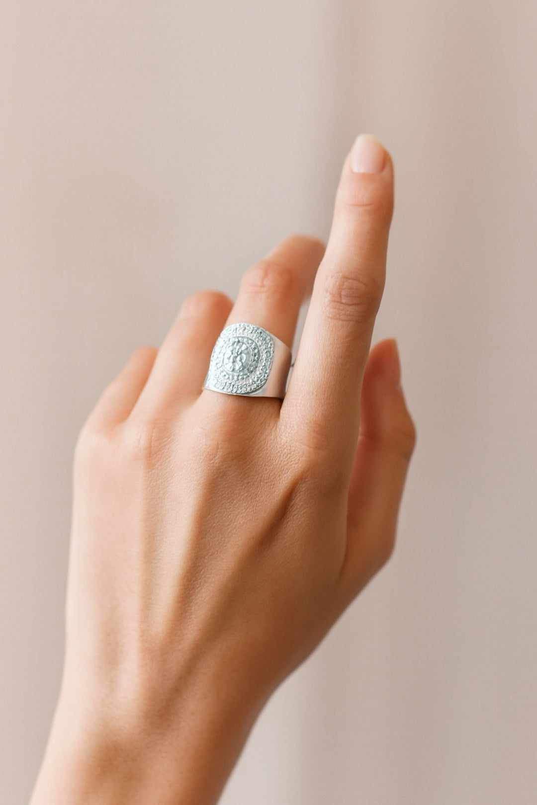 Hand wearing a silver ring with a detailed design on a beige background