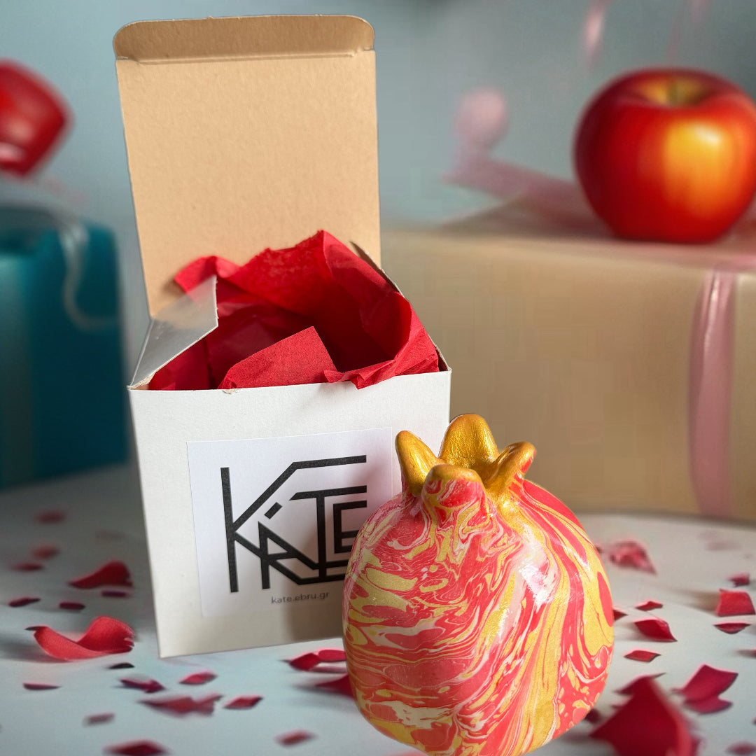 Decorative pomegranate-shaped object with red and gold design in front of an open gift box with red tissue paper.
