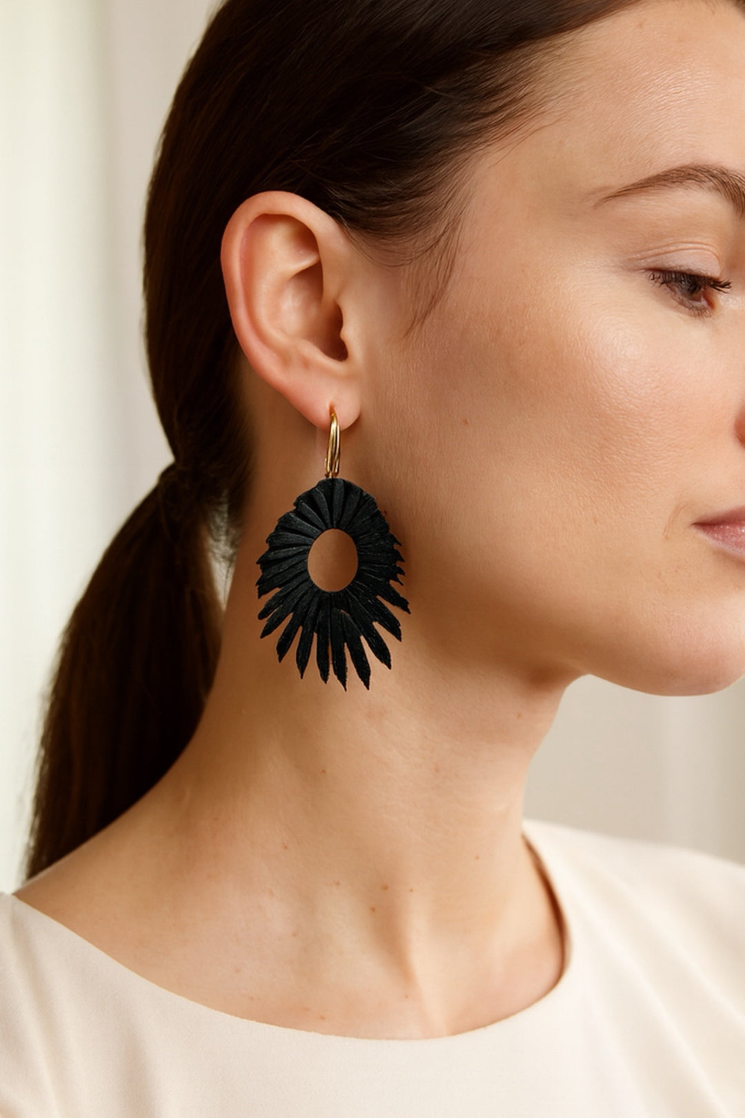 Woman wearing a black floral earring against a neutral background