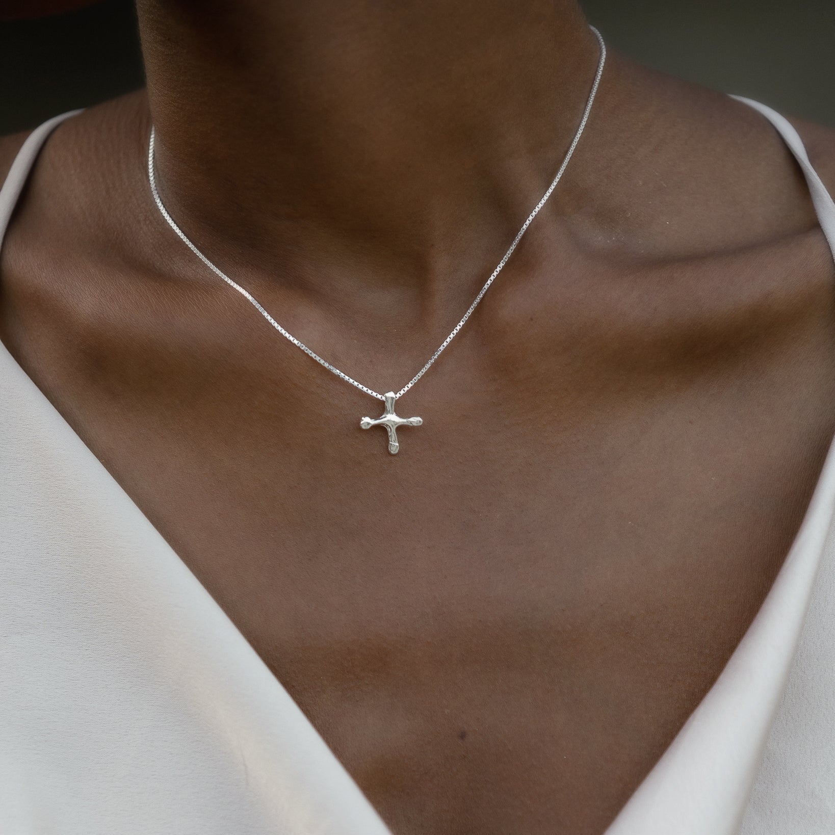 Silver cross necklace on a person wearing a white top