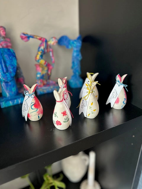 Decorative bunny figurines on a shelf with colorful abstract art in the background.