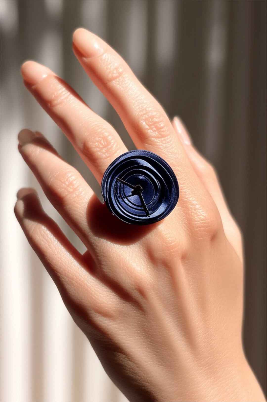Hand wearing a dark blue ring with a floral design against a neutral background