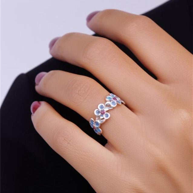 Close-up of a hand wearing a floral silver ring with gemstones on a black background