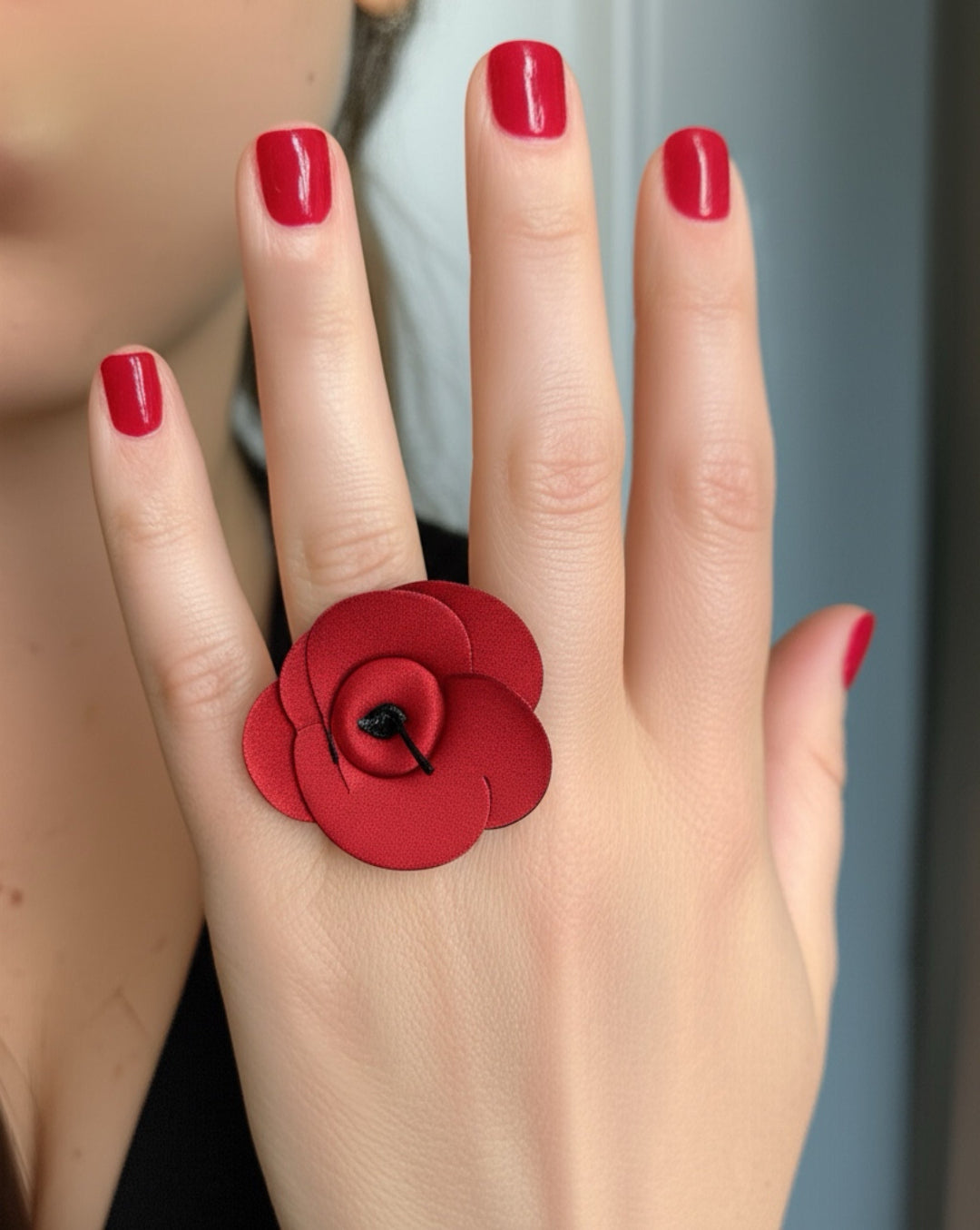 Red flower ring on a hand with red nail polish against a neutral background