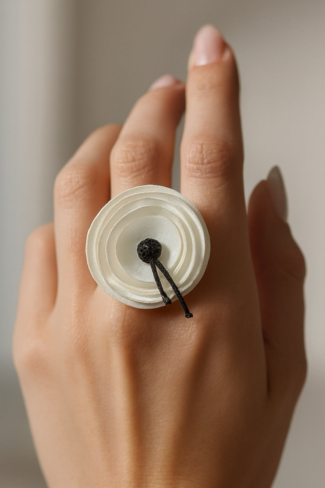 Close-up of a hand wearing a unique white ring with a black center on a neutral background