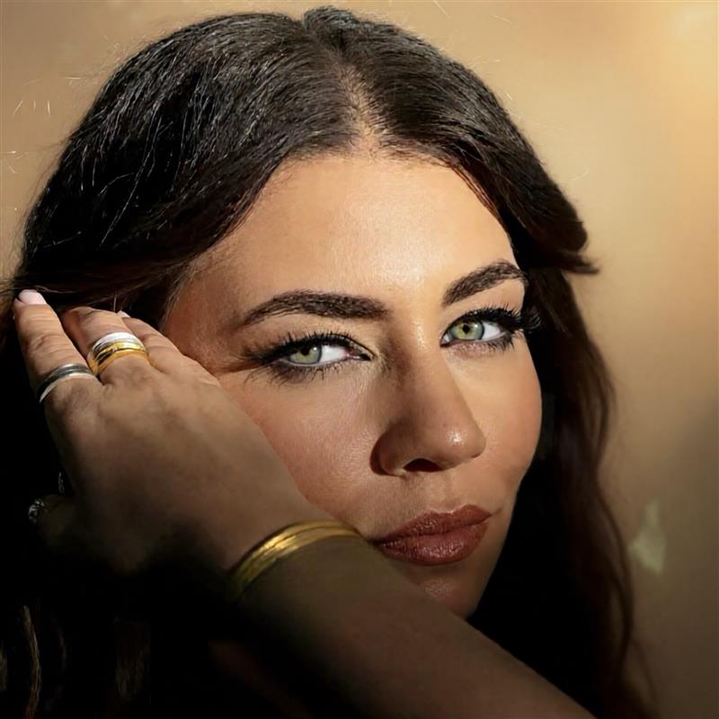 Woman with green eyes and dark hair, with a hand touching her hair against a beige background