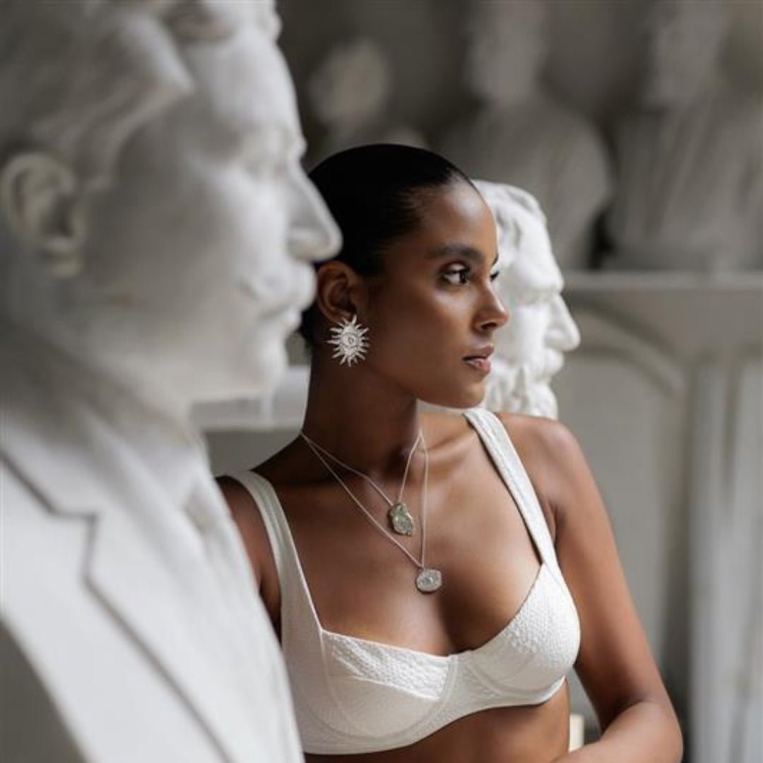 Woman in a white bra and pants standing among classical statues