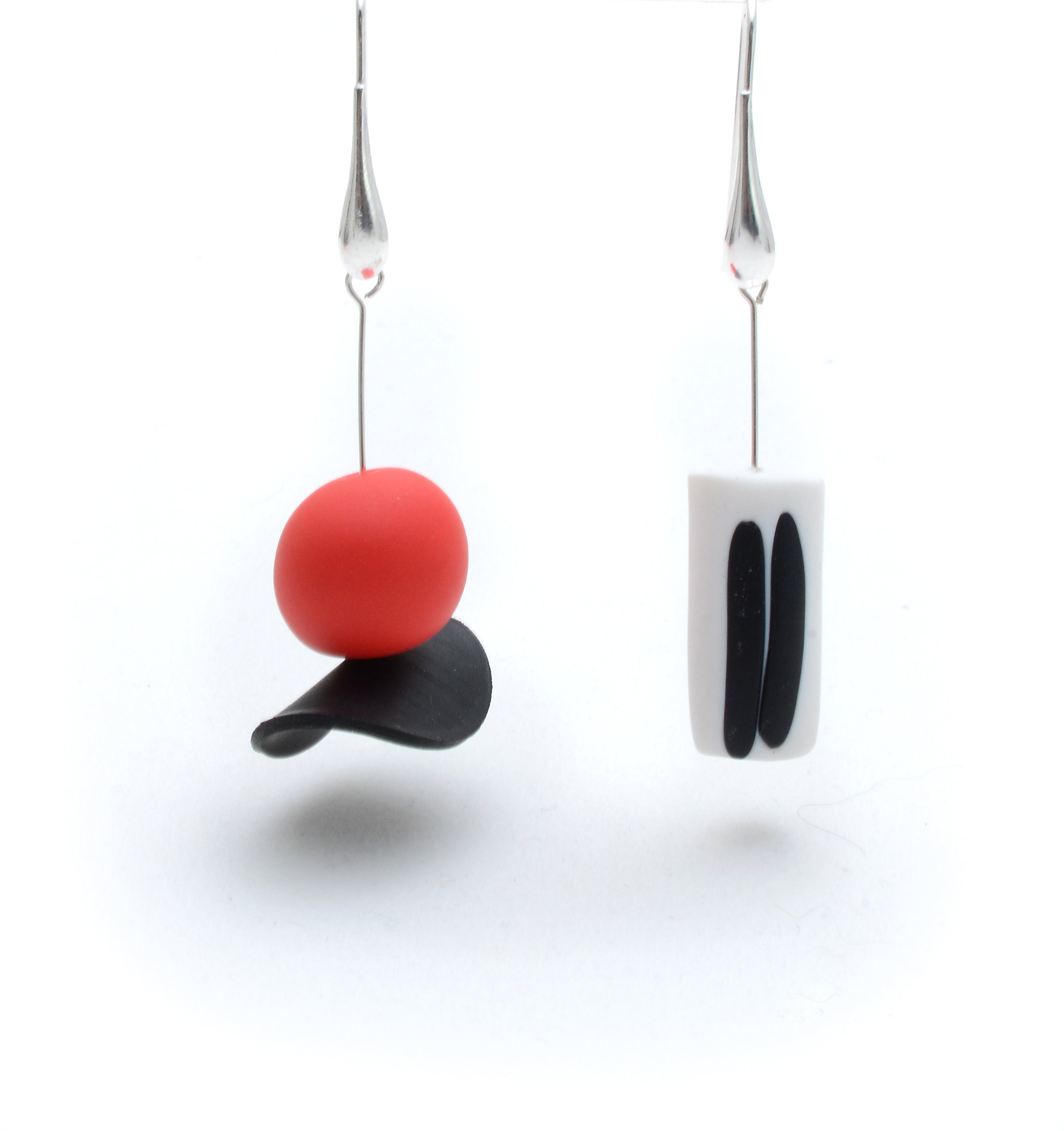 Pair of earrings with a red sphere, black leaf, and white square design on a white background