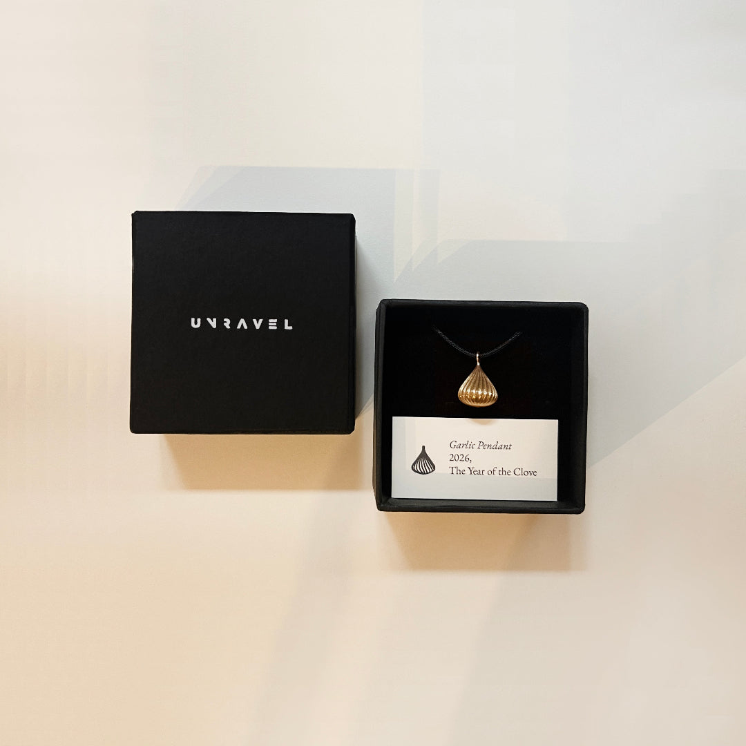 Gold pendant necklace in a black box with 'Unravel' branding on a light background