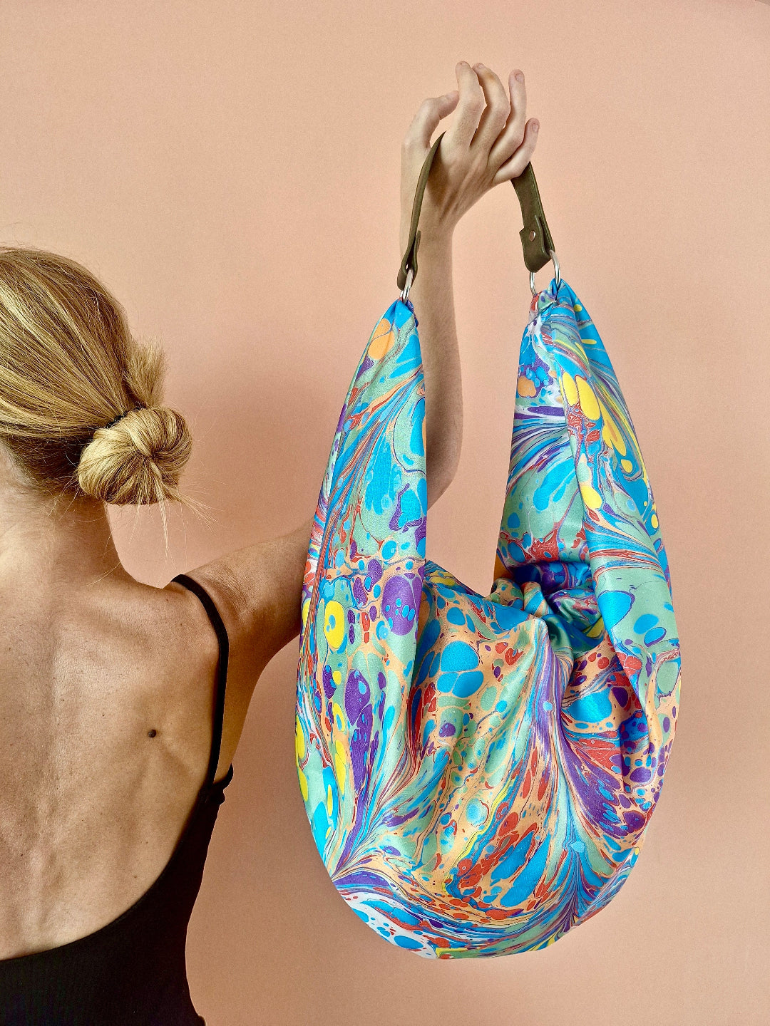 Woman holding a colorful marbled bag against a beige background
