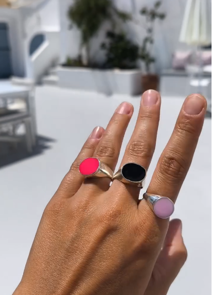 Hand wearing three rings with different colored stones against a blurred outdoor background