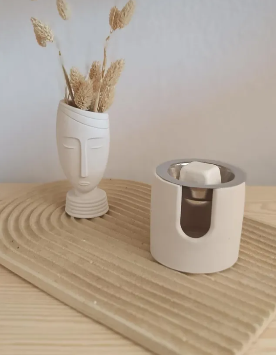 White ceramic vase with dried plants and a white candle holder on a wooden surface.