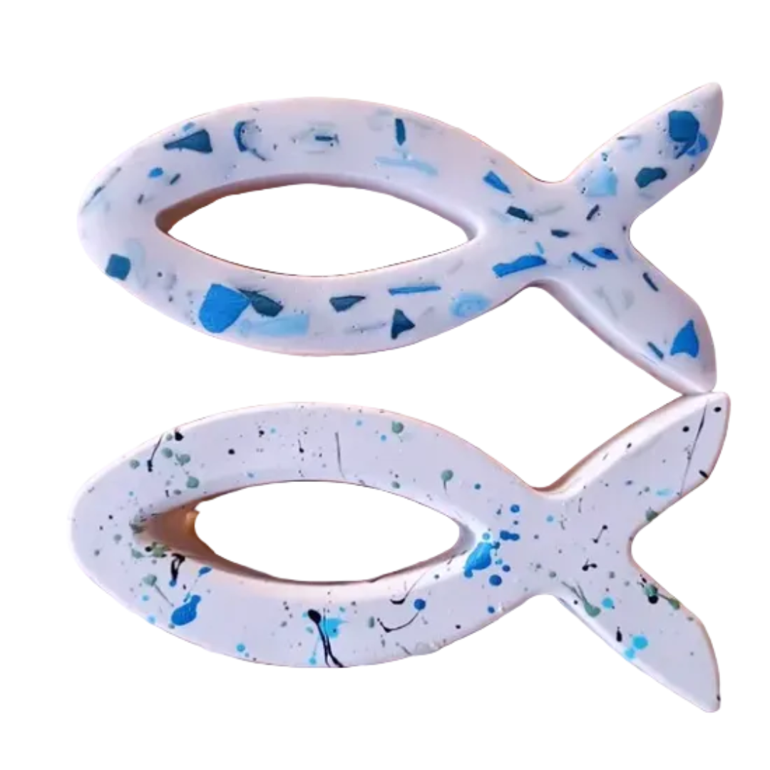 Two white fish-shaped objects with blue and black speckles on a white background