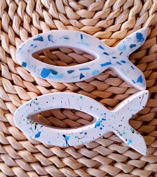 Two white fish-shaped objects with blue and black speckles on a woven surface