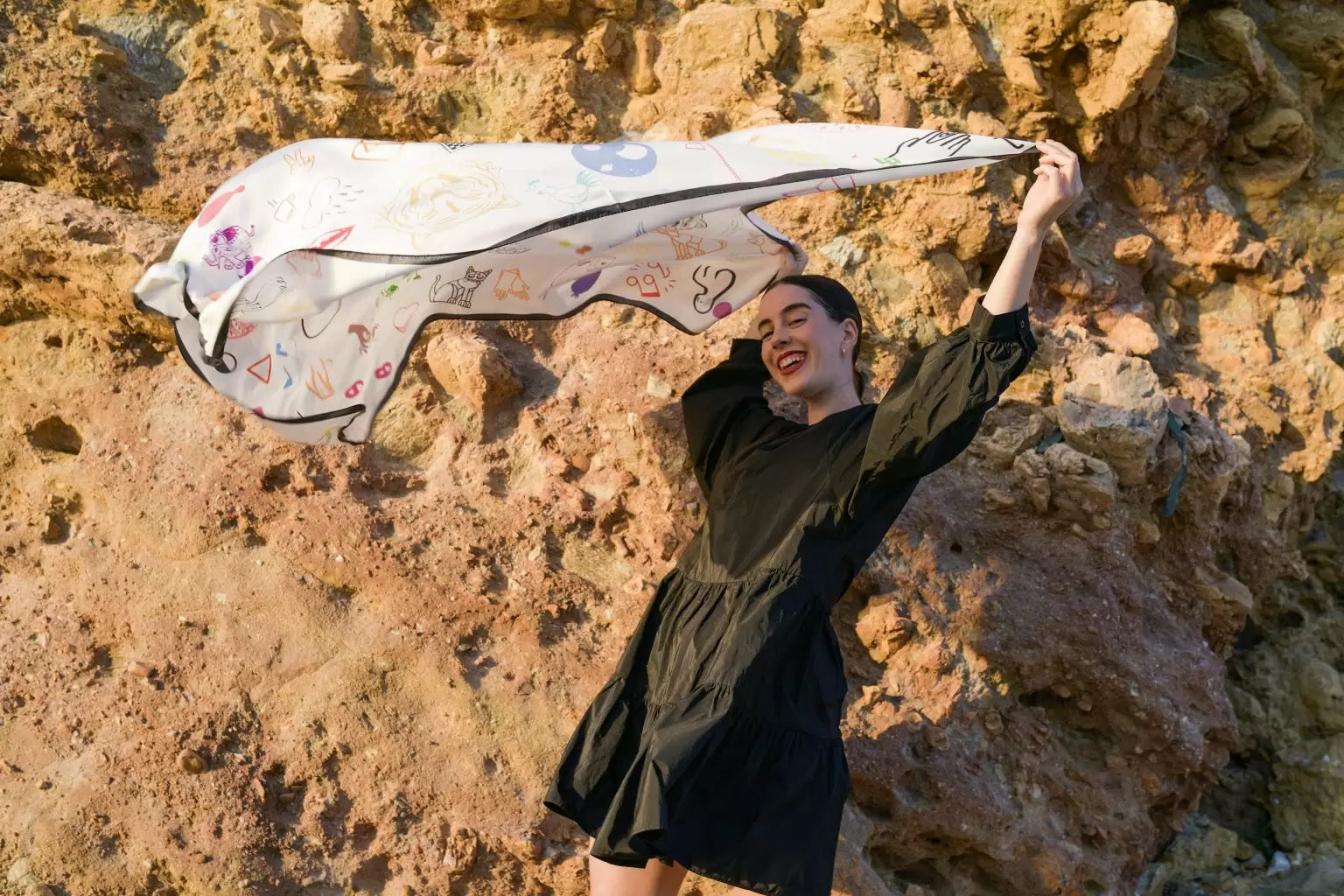 Woman holding a patterned scarf against a rocky background