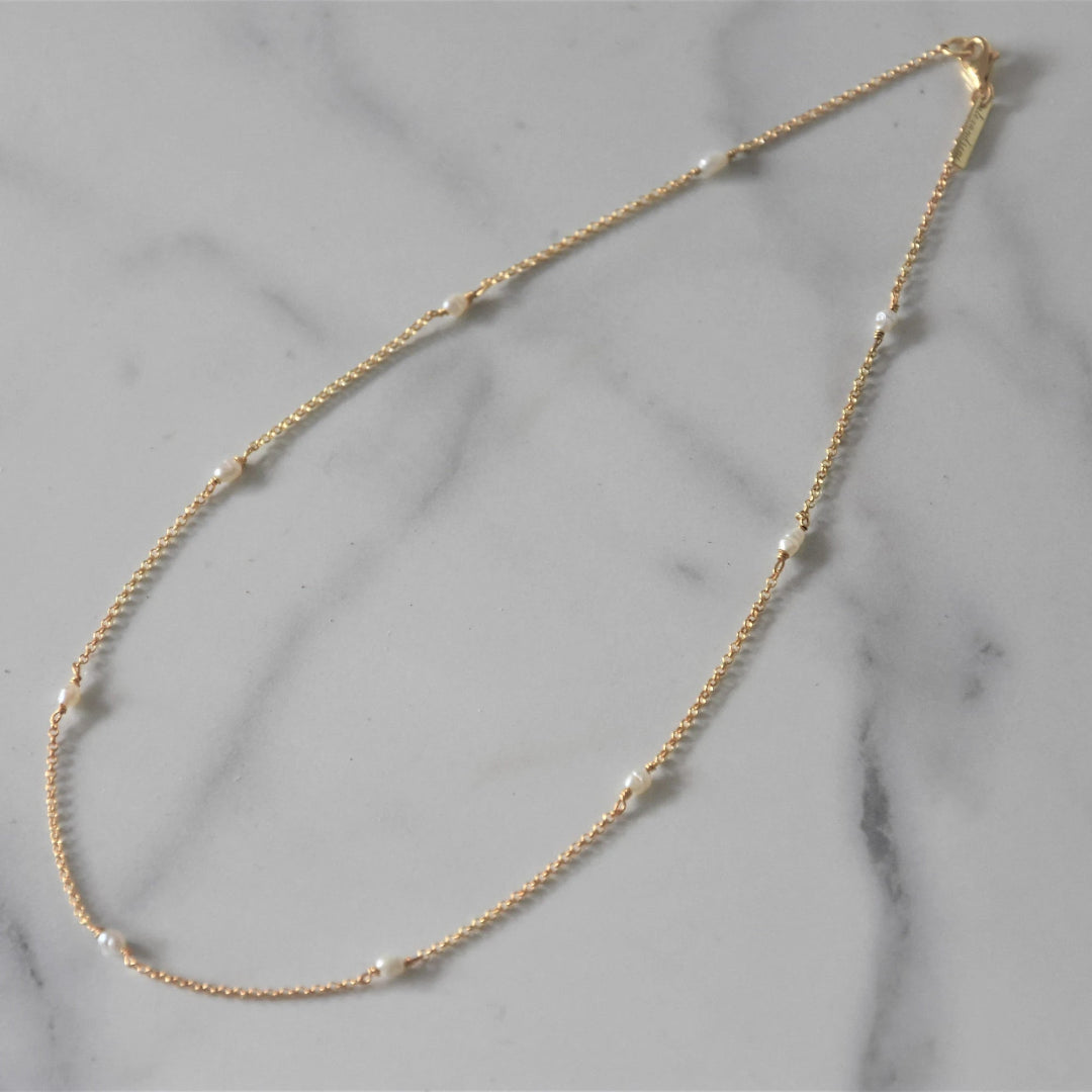 Gold chain necklace with small pearls on a marble surface