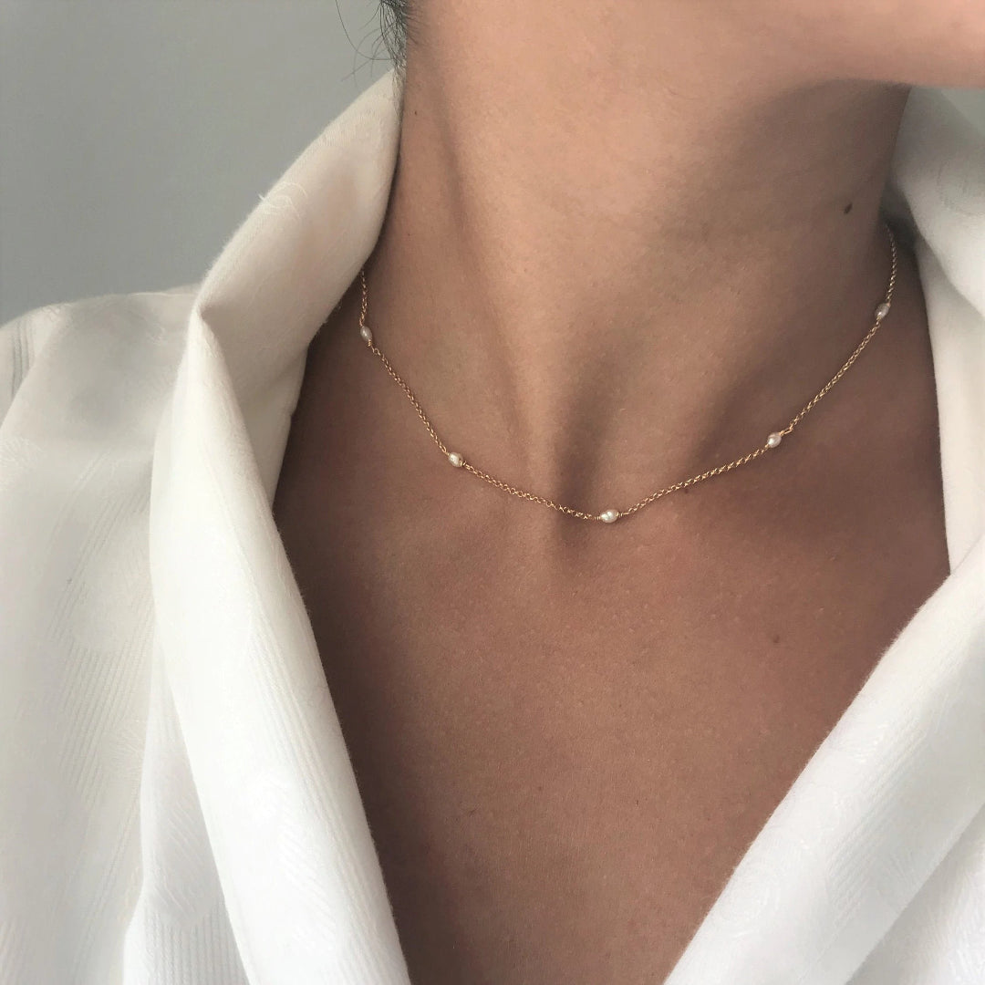Necklace with small beads worn by a person in a white outfit against a neutral background