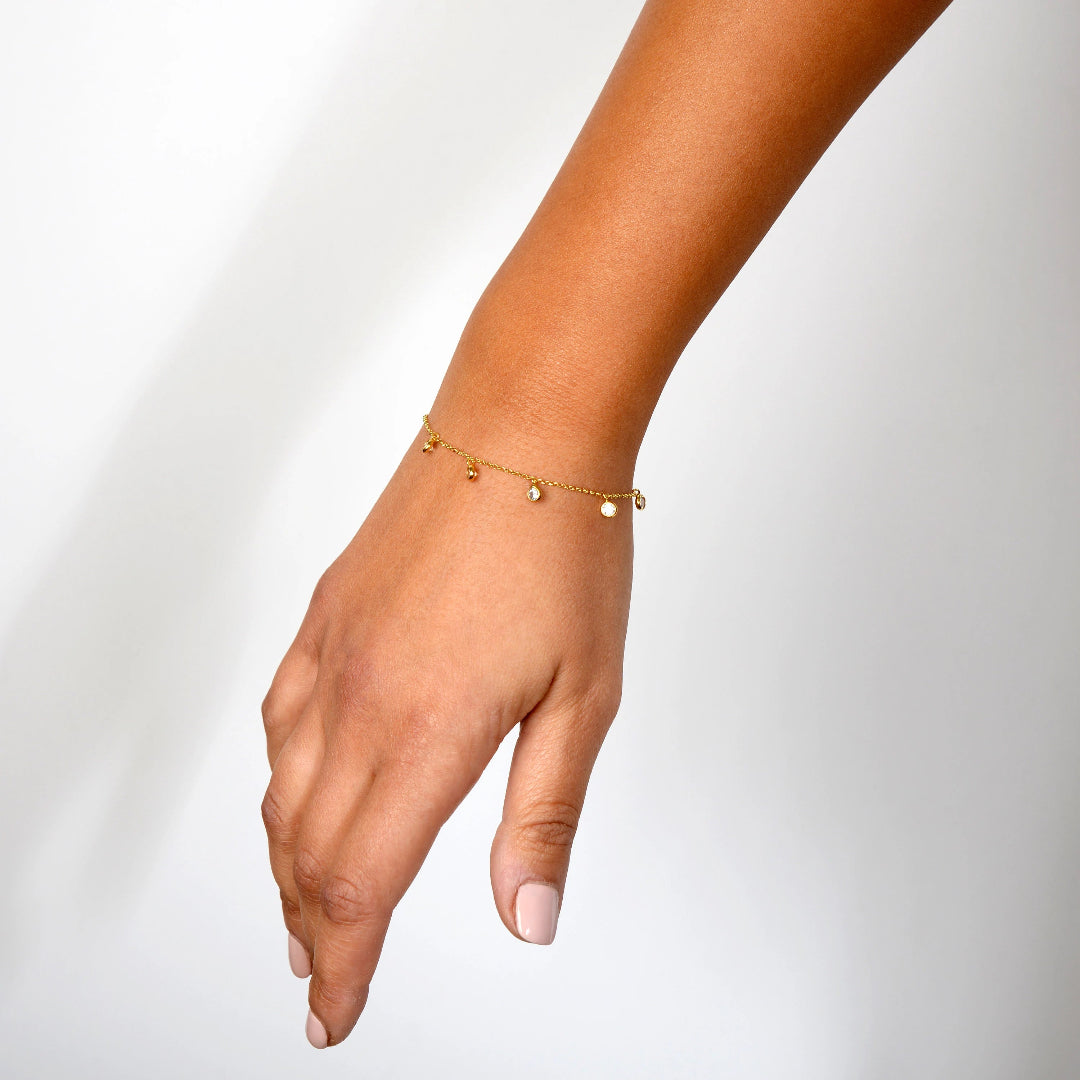 Hand wearing a gold bracelet on a plain background