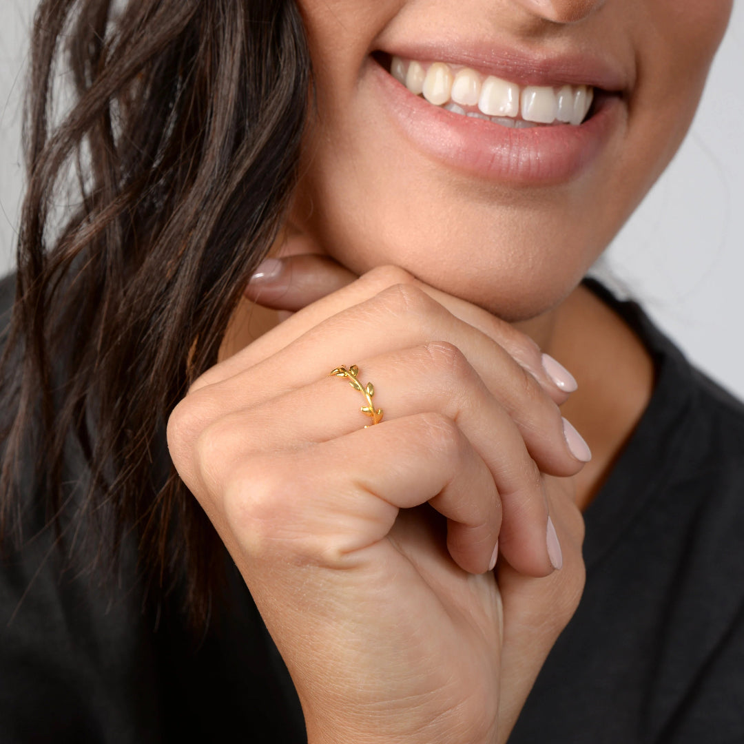 Close-up of a woman's hand with a gold ring, wearing a black top against a neutral background