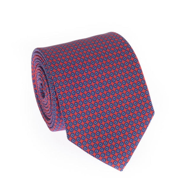 A rolled silk necktie featuring a repeating geometric pattern of concentric circles in navy blue, burgundy, and red, set against a plain white background.