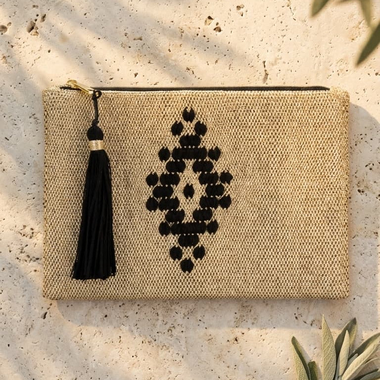 Textured pouch with black geometric design and tassel on a textured surface with leaves.