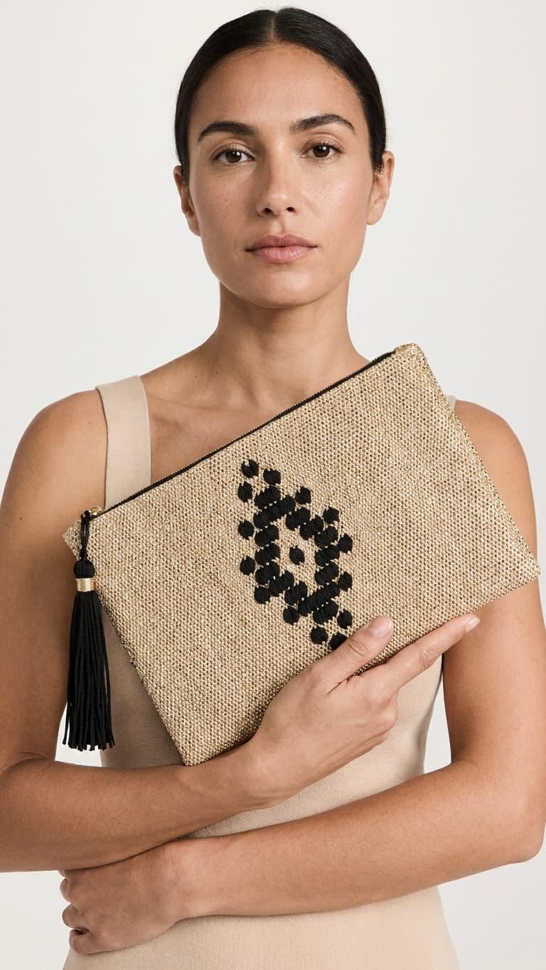 Woman holding a beige clutch with black beading and tassel on a white background