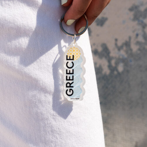 Keychain with 'Greece' text held by a hand on a light background