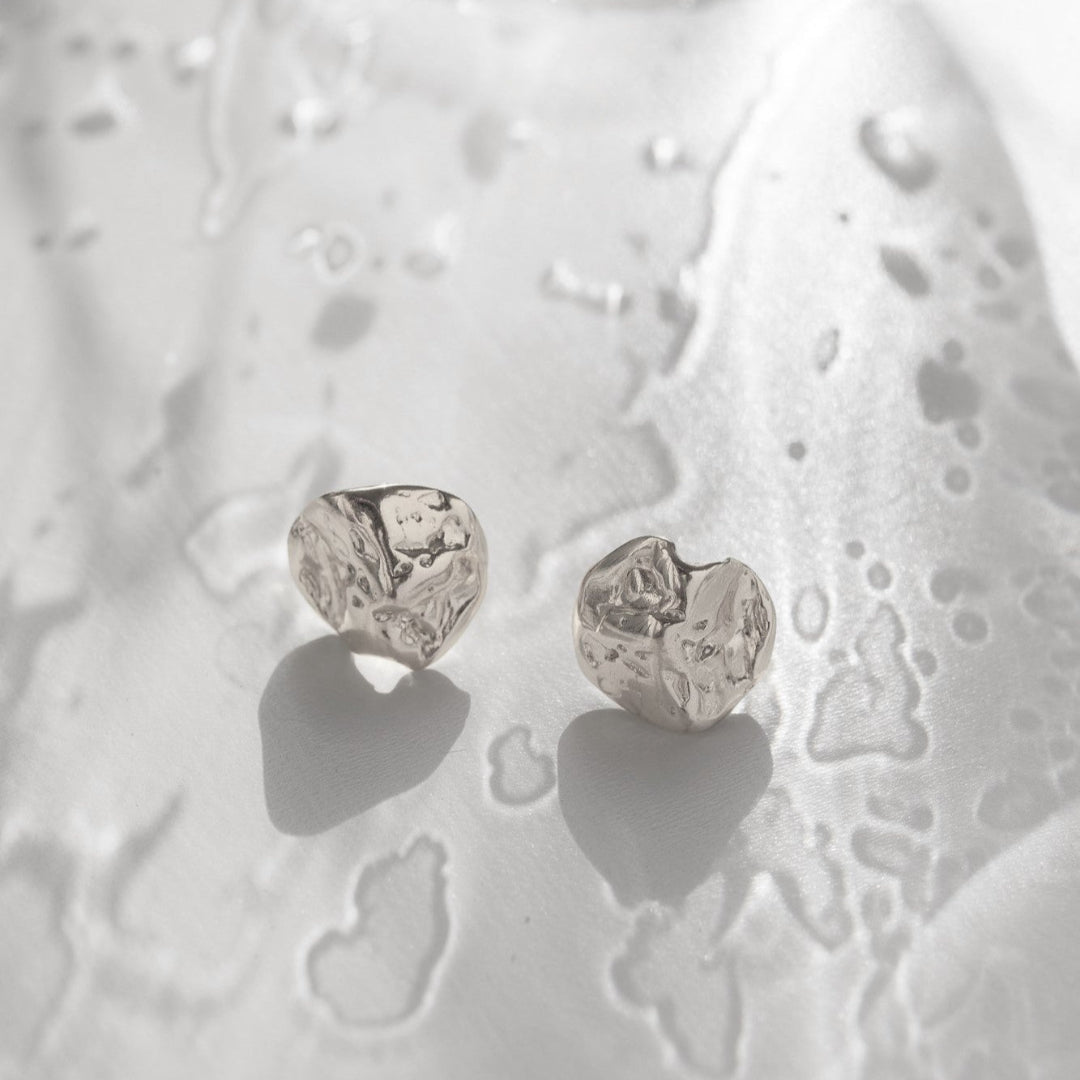 Silver heart-shaped earrings on a textured white surface